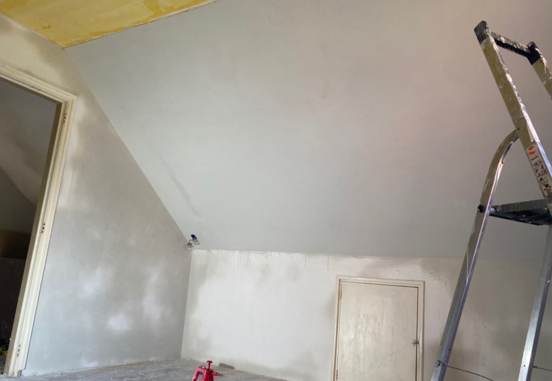 Zolderkamer met schuine wanden, net gestuct, met een trapladder
